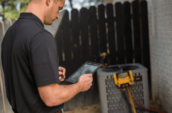 HVAC-service-professional-looking-at-tablet-on-side-of-home