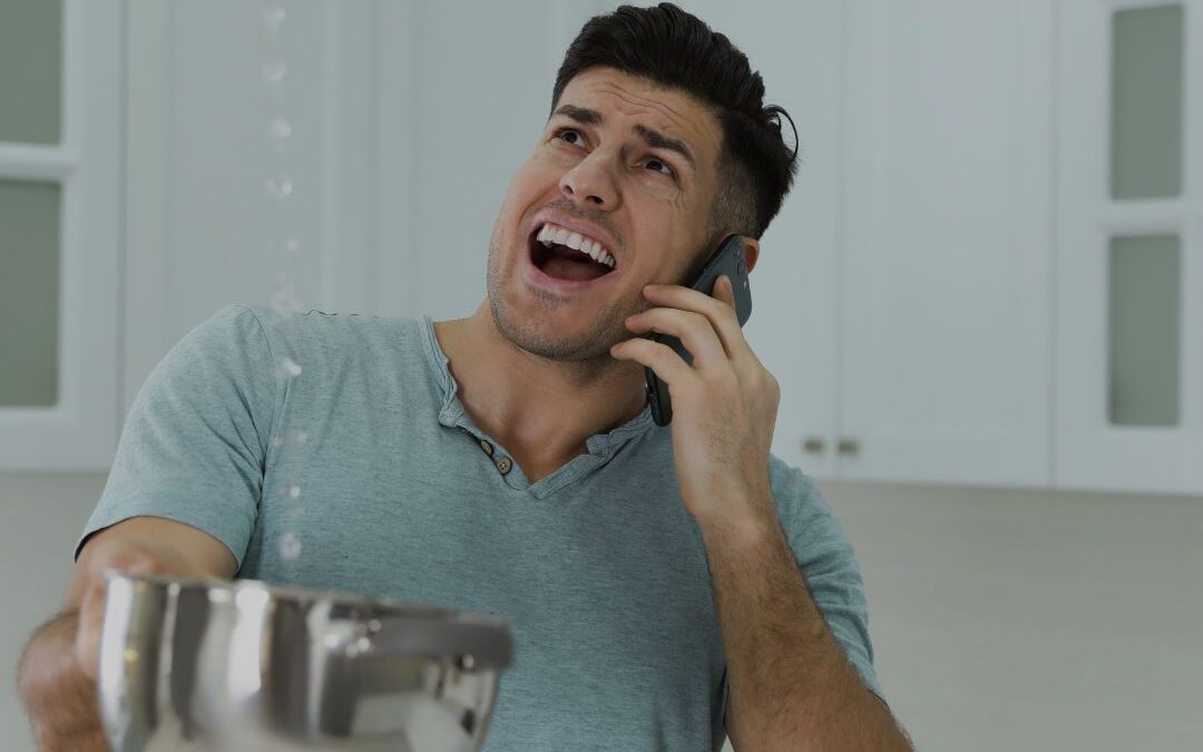 man-on-phone-while-holding-pot-to-catch-water-dripping