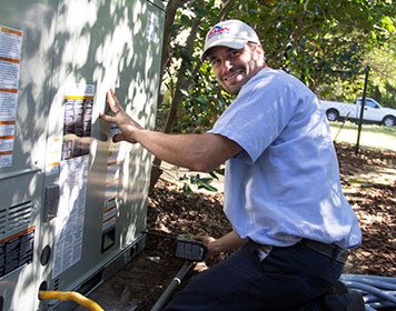 Smoaks_Technician hvac-tech-in-front-of-unit-on-side-of-brick-home