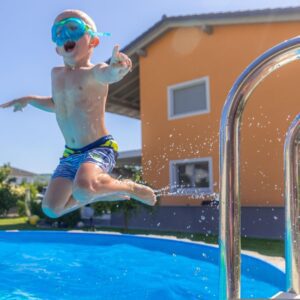 Young-Boy-in-Swim-Googles-and-Bathing-Suit-Jumping-in-Pool